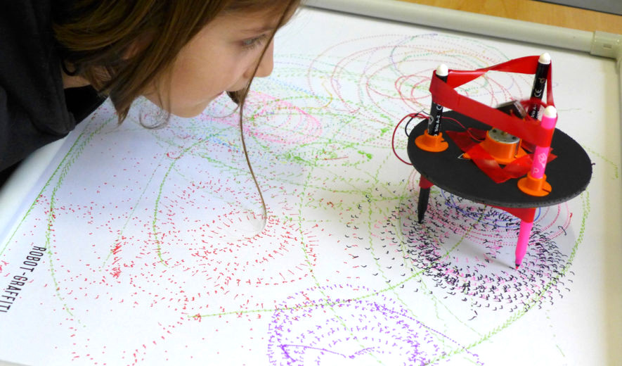 une enfant regarde un robot dessiner sur une grande feuille